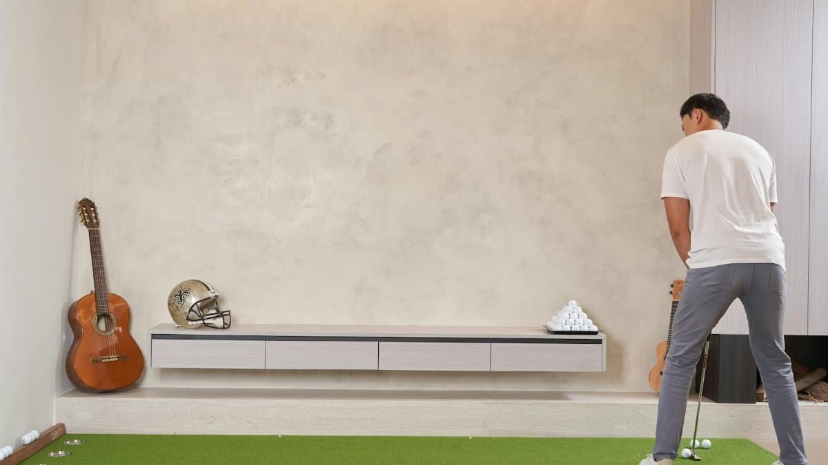 Man practicing golf indoors using a putting mat surrounded by decor.