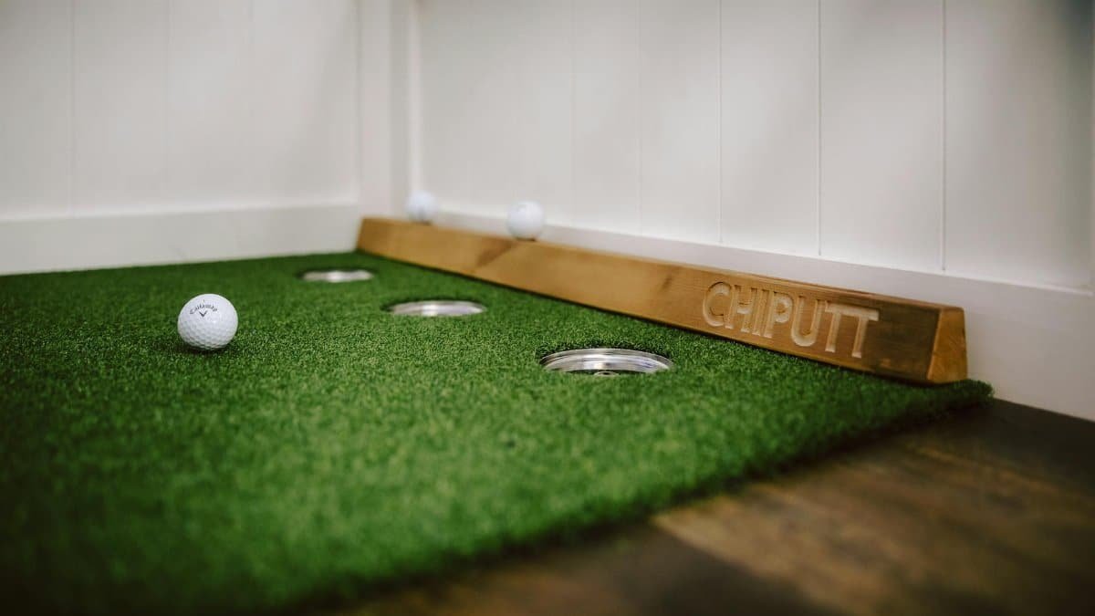 Indoor putting green with golf balls and training aid for golf practice.