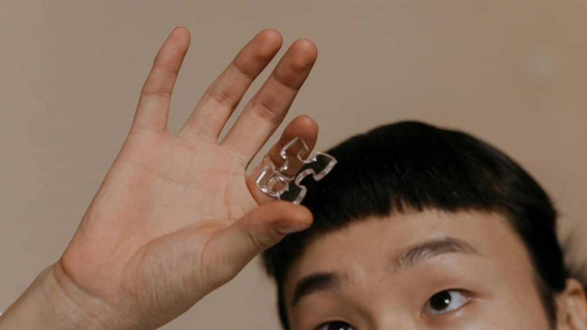 Person holding a transparent puzzle piece, focusing on the hand and expression.
