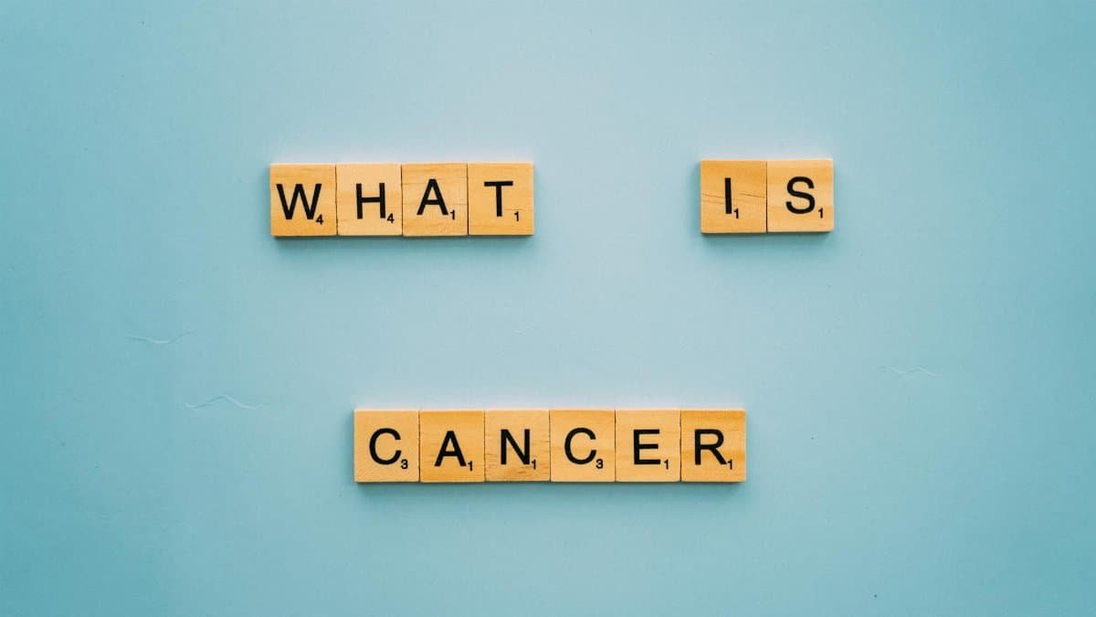 Wooden letter tiles form the question 'What is cancer?' on a blue background.