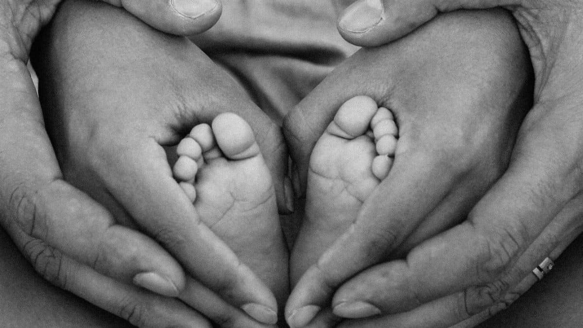 Black and white photo of adult hands cradling baby feet, symbolizing family love and connection.