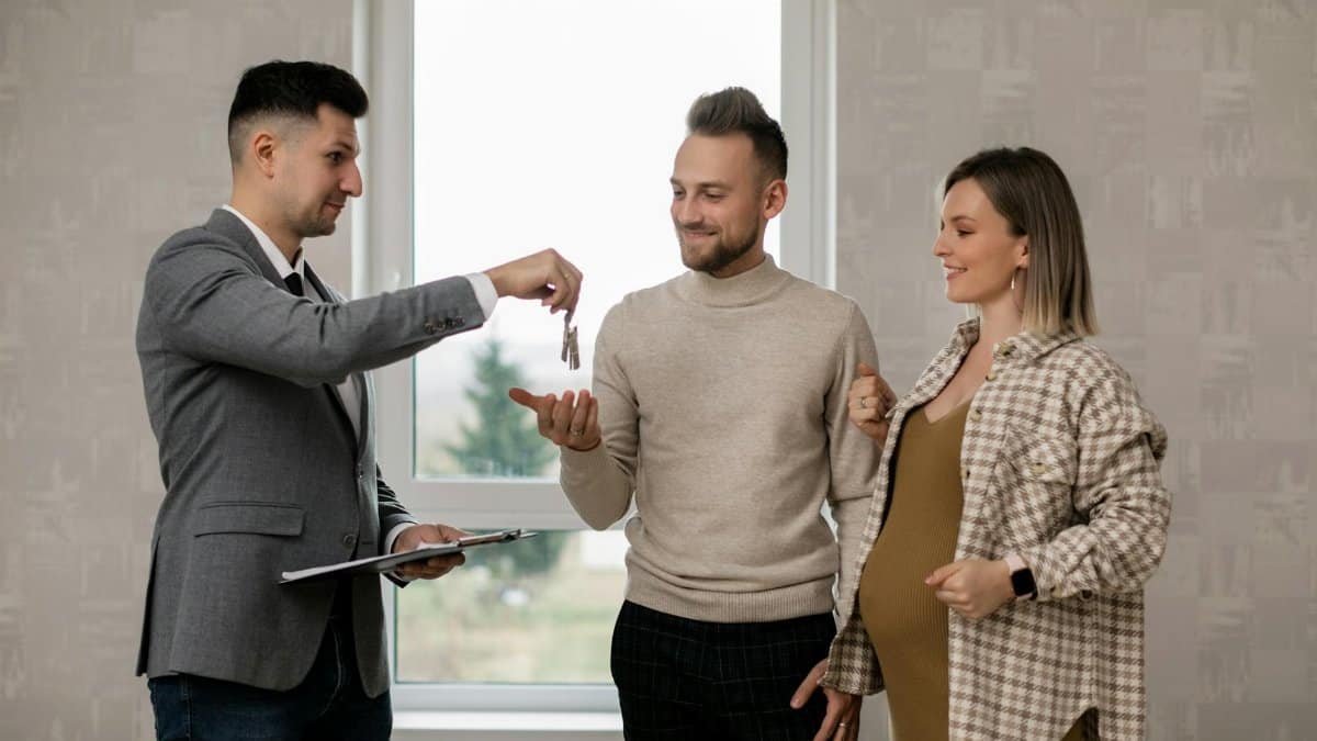 A pregnant woman and her partner receive house keys from a real estate agent indoors.