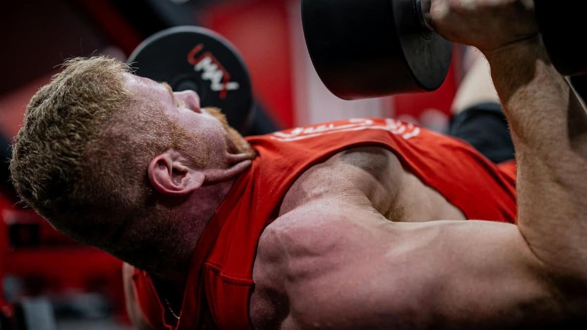 Muscular man performing a dumbbell press workout, focusing on strength and endurance.