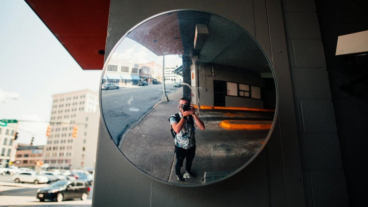 Reflection of a photographer in a city street mirror, capturing urban life.