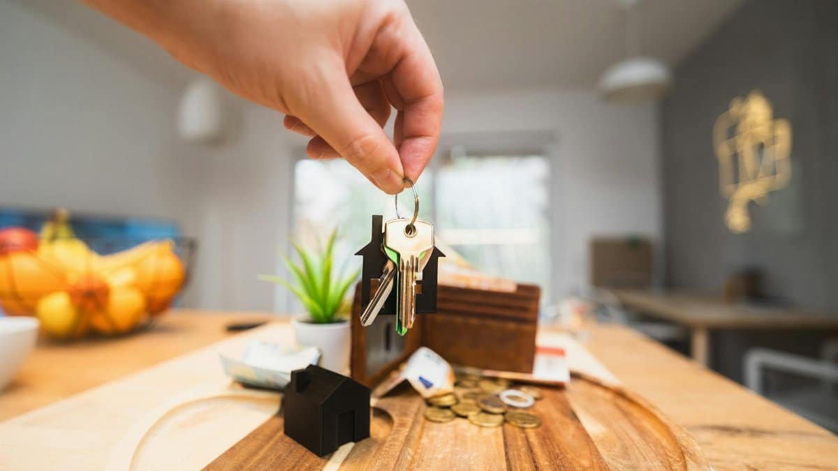 Hand holding keys in a modern living room setting, symbolizing home ownership or real estate investment.