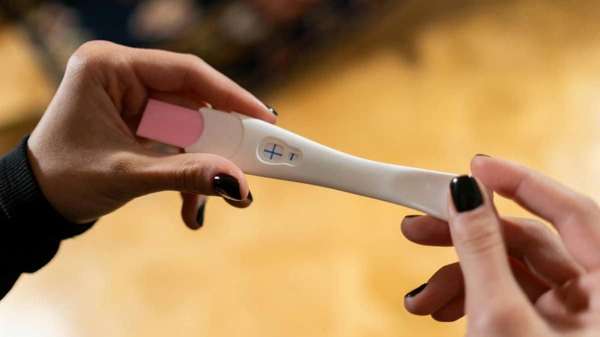 Closeup of hands holding a positive pregnancy test with a cross symbol.