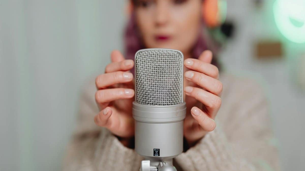 A woman in headphones uses a studio microphone for ASMR recording indoors.