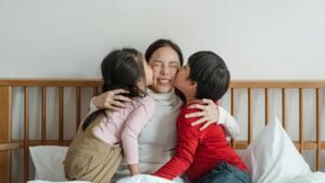 Happy mother embraced by children on bed, sharing joyful bonding moments indoors.