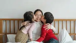 Happy mother embraced by children on bed, sharing joyful bonding moments indoors.