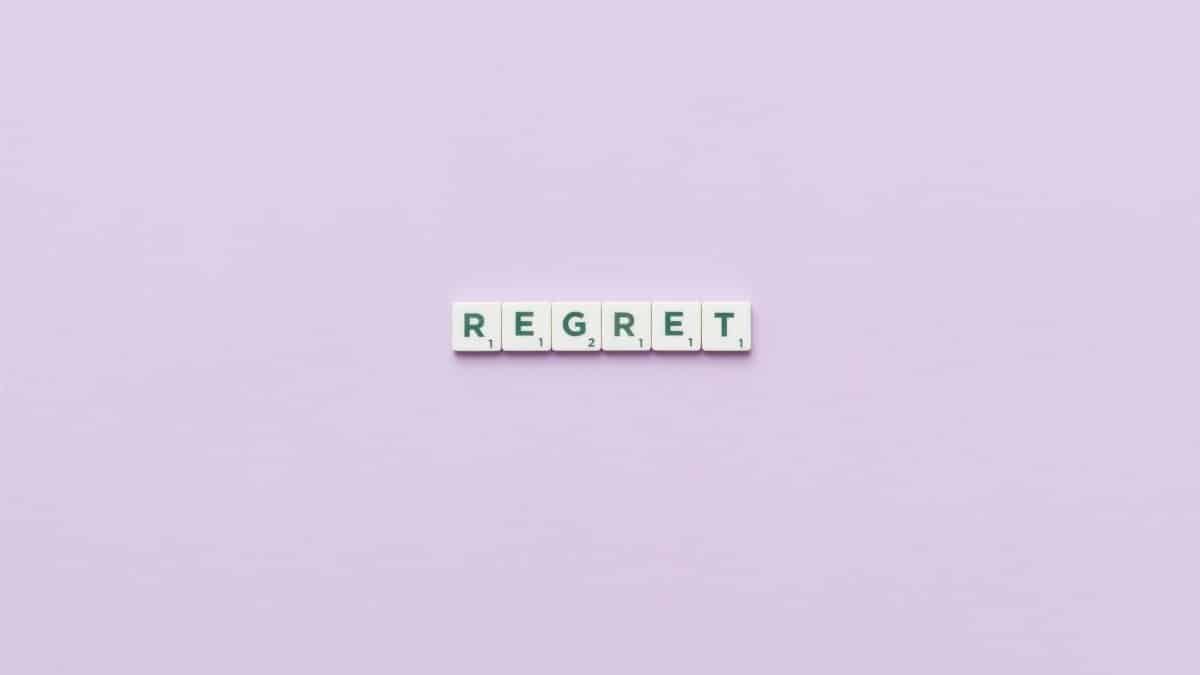 Scrabble tiles forming 'Regret' on a soft pink background, conveying a conceptual theme.