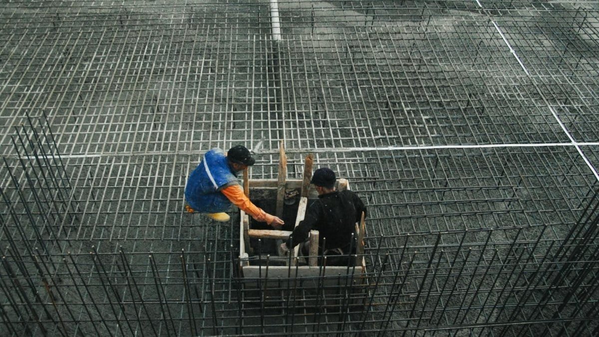 Two workers operating on a construction site with steel frameworks and concrete. High-angle view captures teamwork and industry.