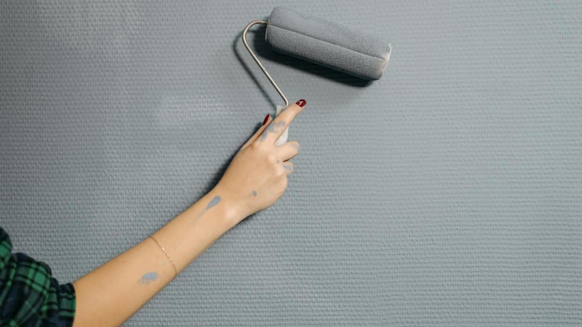 A close-up of a person's hand using a paint roller on a blue wall for home renovation.