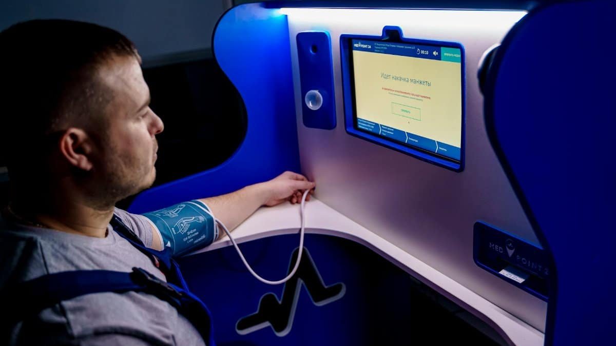 Man measuring blood pressure with a digital monitor at a self-service kiosk for telemedicine.