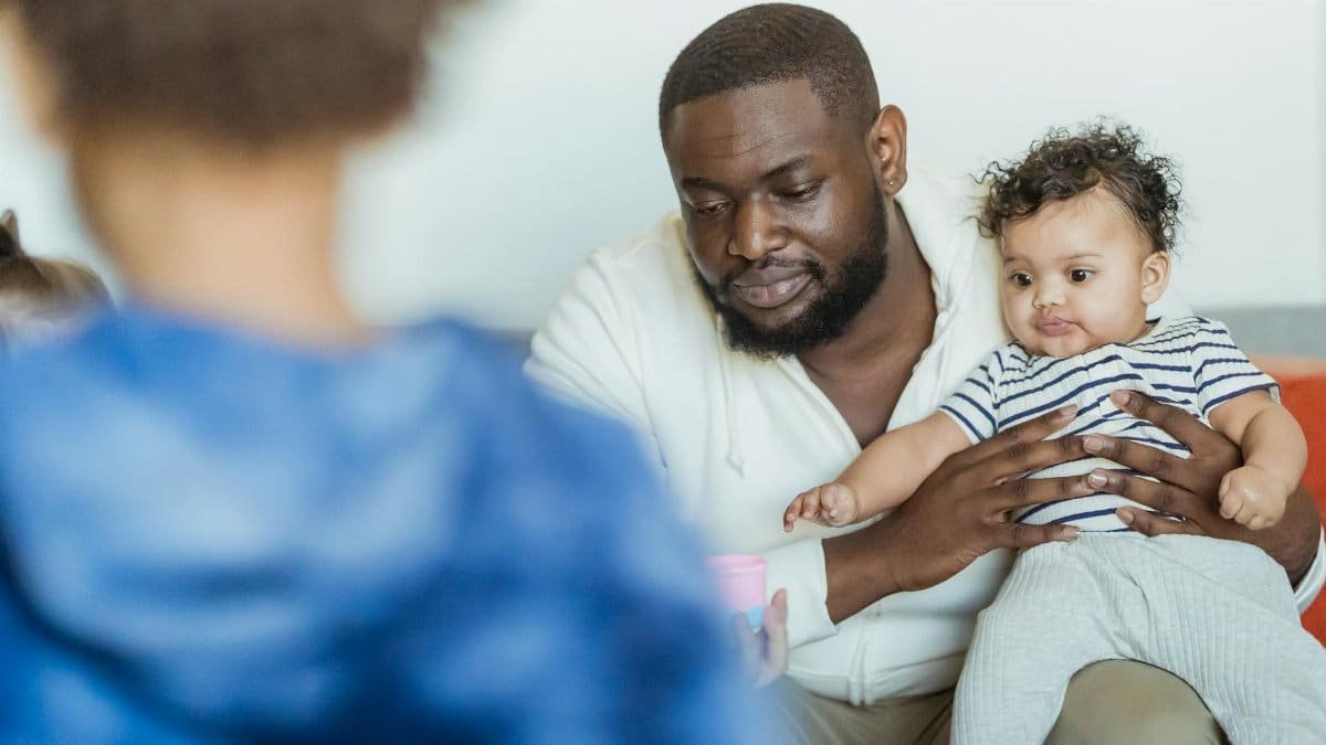 Masculine African American dad with cute toddler child and crop anonymous boy in house room