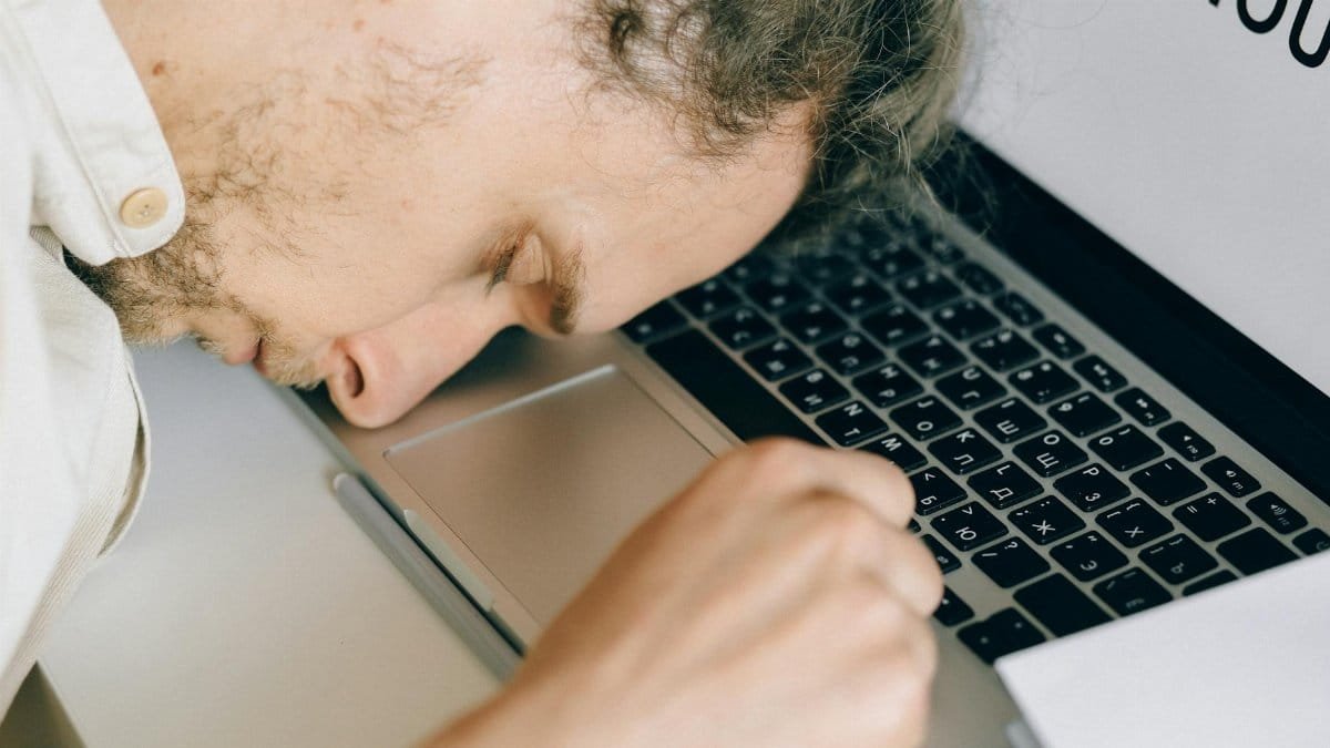 Exhausted employee resting head on laptop keyboard due to burnout and stress.