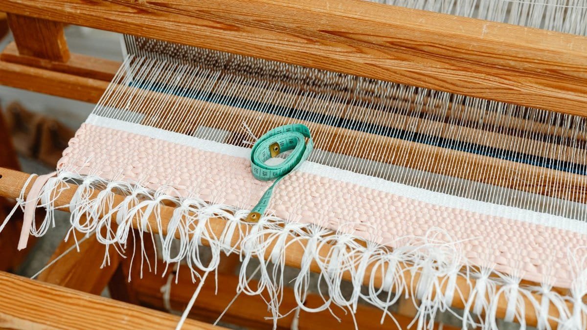 Detailed view of a wooden loom with woven fabric and a measuring tape, highlighting traditional weaving.