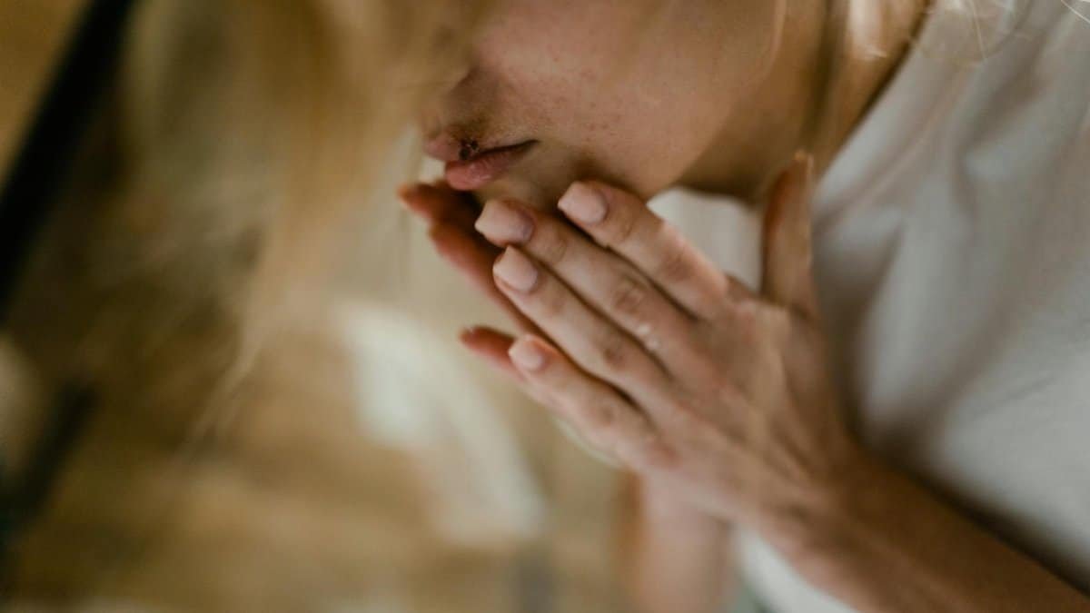 A close-up of a woman's face showing a bruise and hands touching her lips, indoors.
