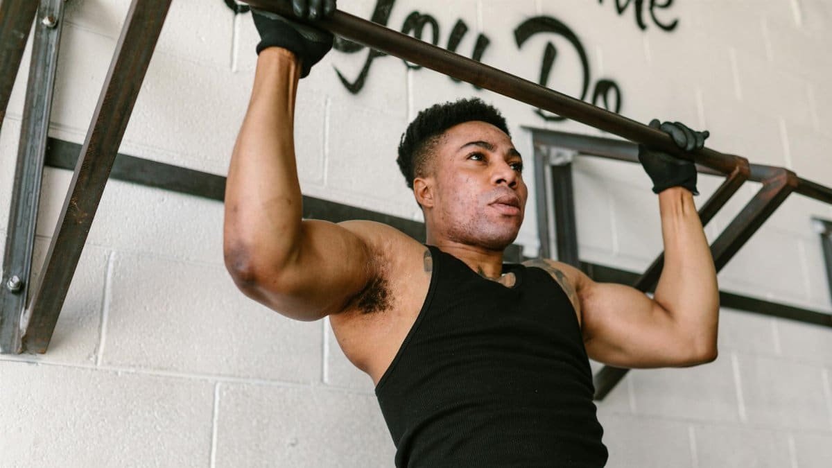 Athletic man doing pull-ups in a gym setting, showcasing strength and fitness.