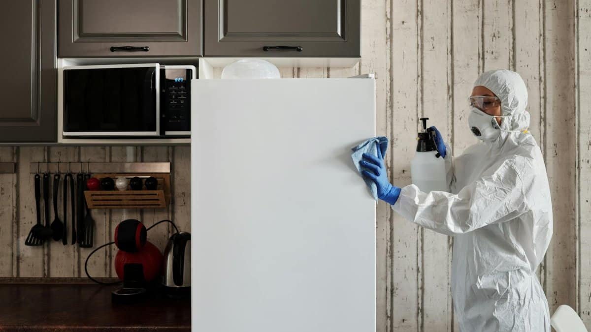 A person in protective gear cleaning a kitchen appliance to ensure hygiene.