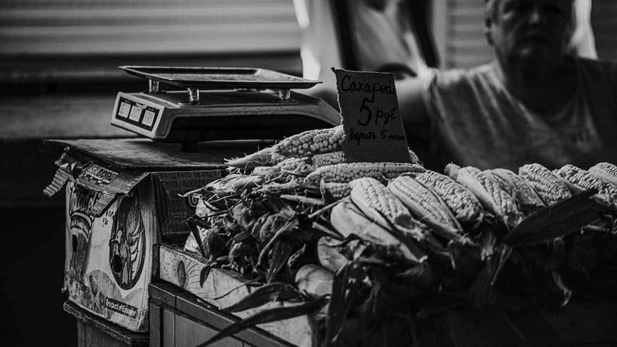 Black and white image of a market stall with corn and a vintage scale.