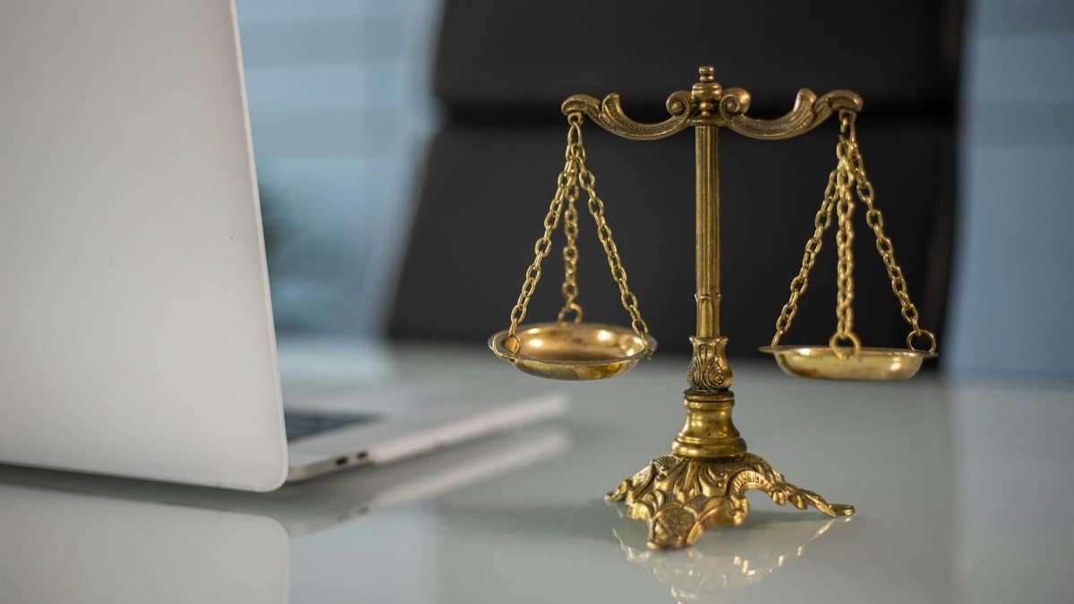 Golden justice scales on a desk beside a laptop, symbolizing law and balance.