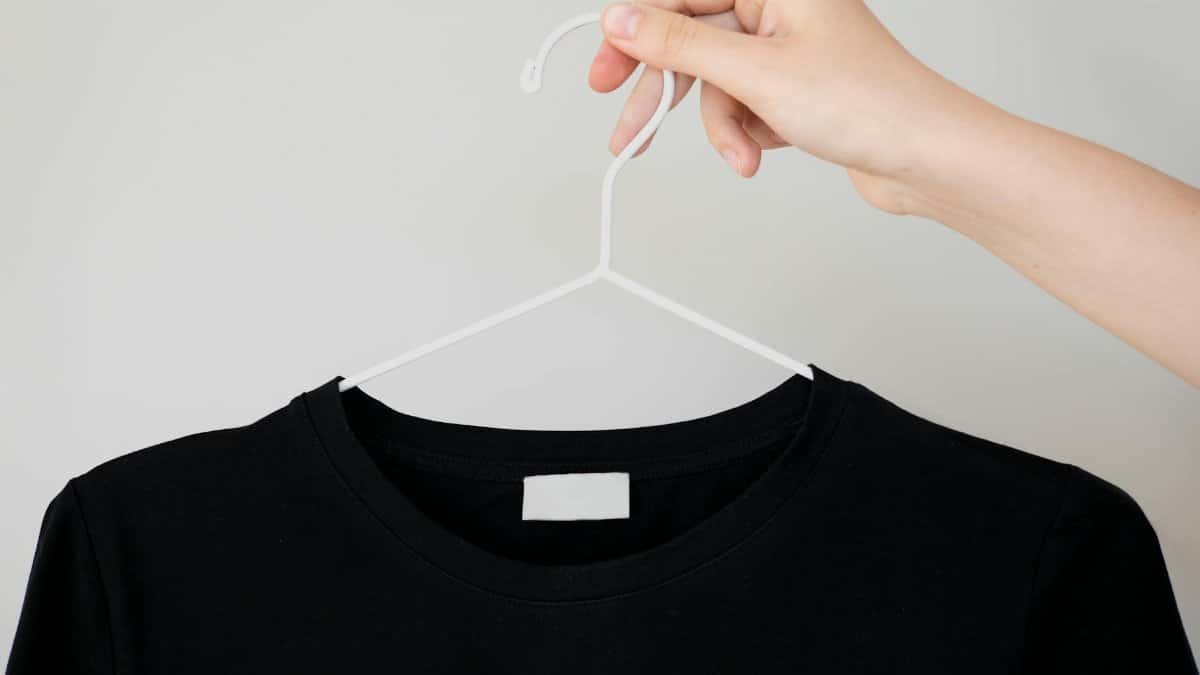 Black t-shirt on hanger with hand holding, perfect for apparel mockups.