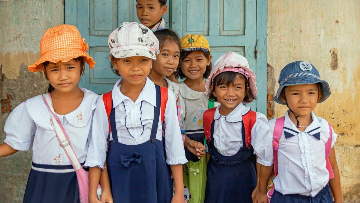 Group of Vietnamese school children smiling in traditional uniforms outside a rustic building.