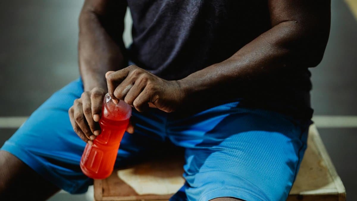 A man resting on a wooden box, enjoying a red sports drink during his workout session.