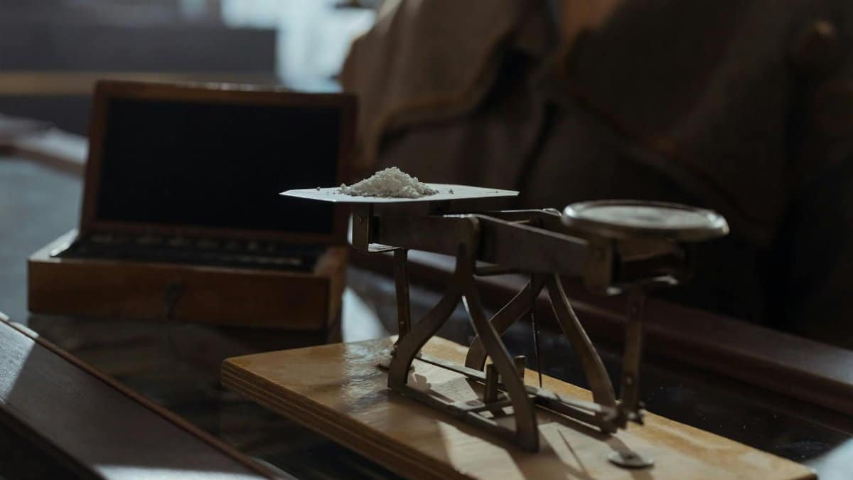 Classic vintage weighing scale with a small heap of white powder placed indoors on a wooden surface.