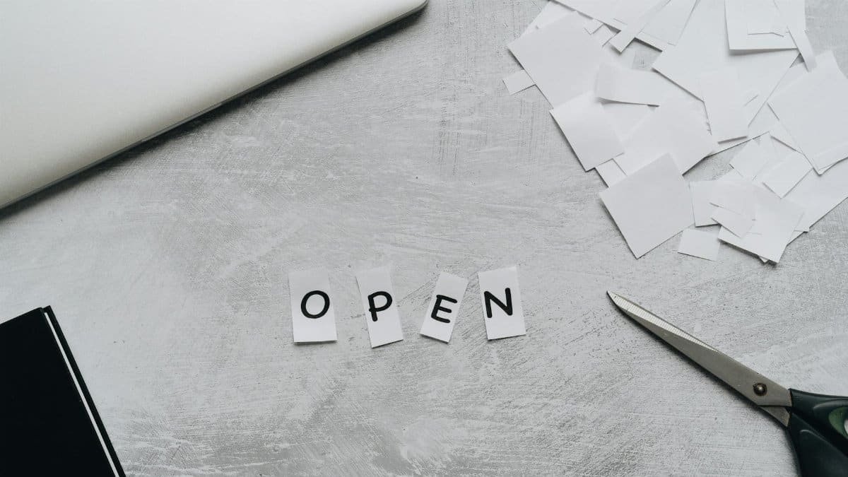 Flat lay of a creative workspace with paper letters spelling 'OPEN,' scissors, and a laptop.