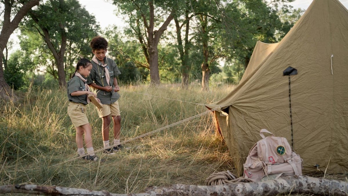 Two children working together to set up a tent in a forest camping scene.