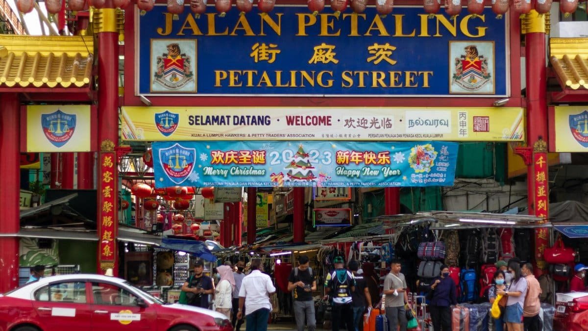 Vibrant scene of Petaling Street in Kuala Lumpur with market stalls and diverse crowd.