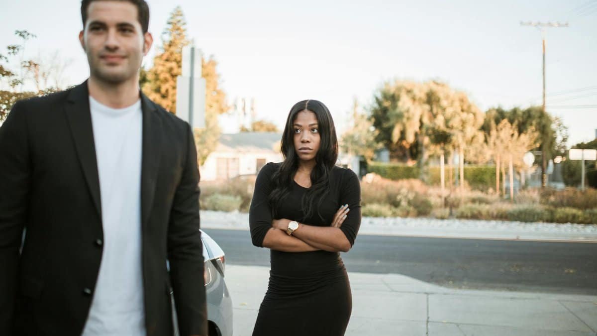A couple facing relationship tension outdoors with arms folded, expressing emotions.