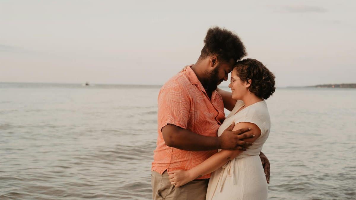 A loving couple embraces on the beach at sunset, showcasing warmth and romance.