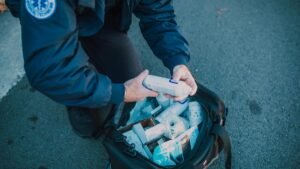 Emergency responder organizing medical supplies from a kit in an outdoor setting.