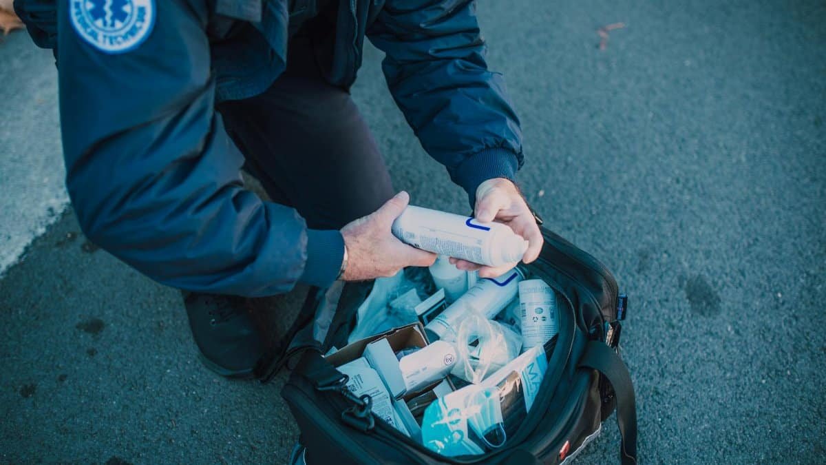 Emergency responder organizing medical supplies from a kit in an outdoor setting.