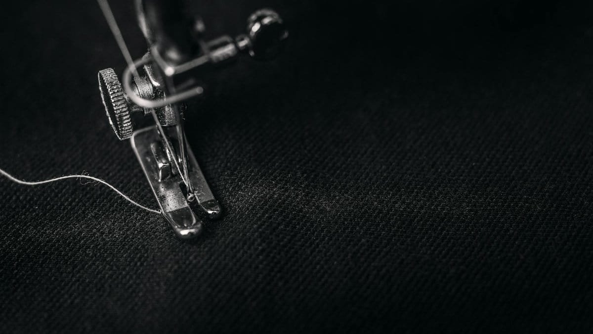 Detailed view of a sewing machine needle stitching fabric, highlighting sewing process and textile technology.