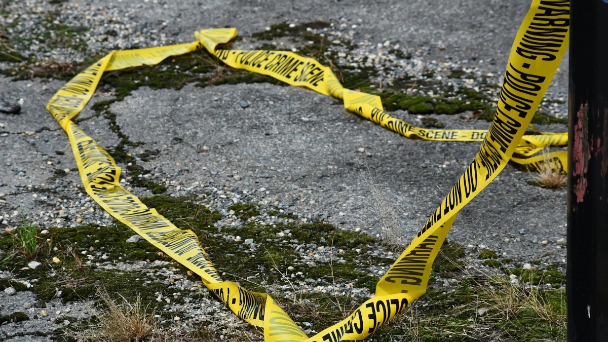 Close-up of yellow police crime scene tape on a cracked and mossy pavement outdoors.