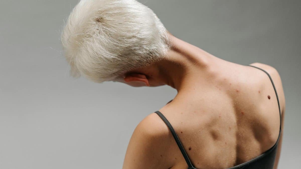 Back view of a woman with white hair bending her neck, showing body movement and detail on gray background.