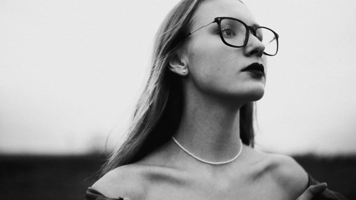 Artistic black and white portrait of a woman wearing glasses and an off-the-shoulder outfit.