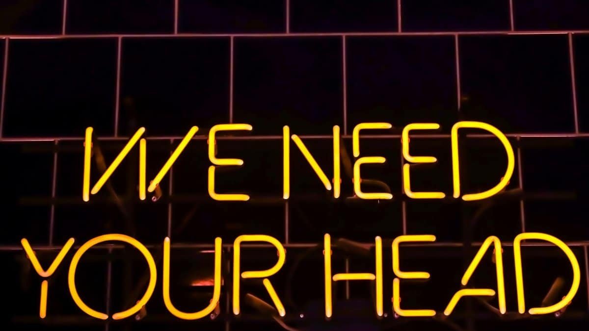 Vibrant neon sign 'WE NEED YOUR HEAD' glowing at night in Riga, Latvia.