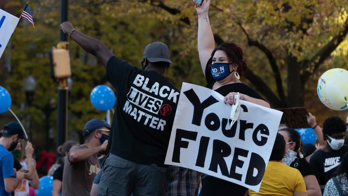 Protesters holding signs during a rally, expressing political views outdoors with colorful balloons.