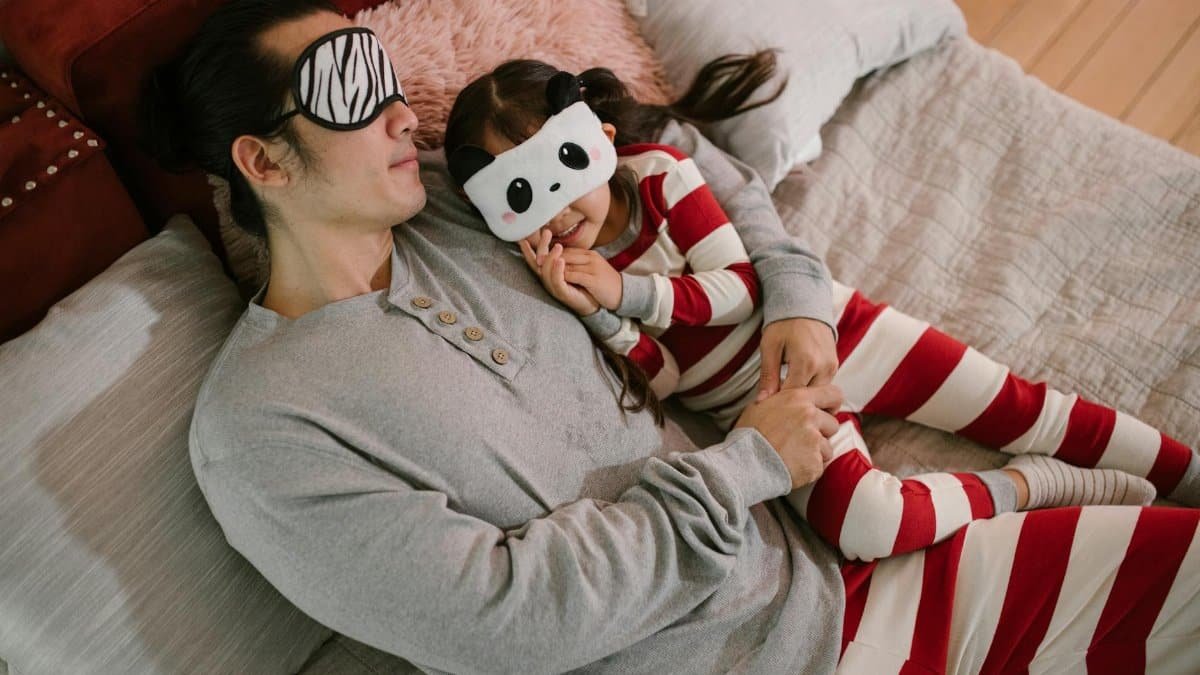 Father and daughter enjoying a cozy bedtime routine with playful sleep masks and striped pajamas.