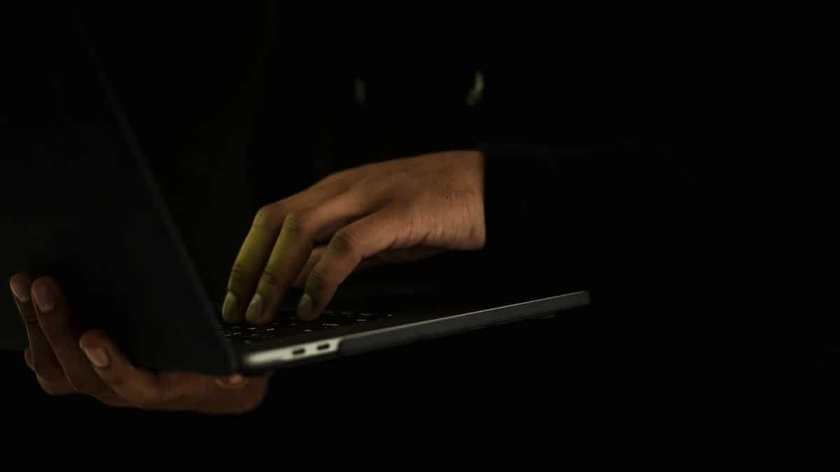 A close-up of a person's hands typing on a laptop in a dark setting, suggesting secrecy or privacy.