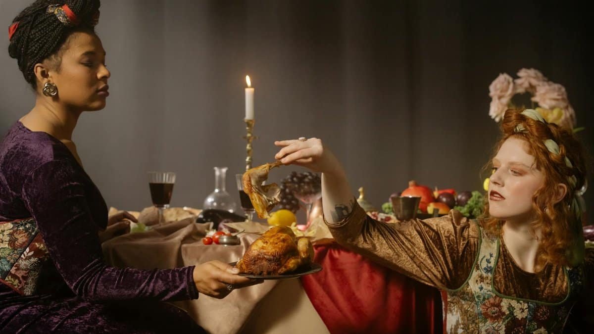 Two women in renaissance costumes sharing a vintage feast, candlelit setting.