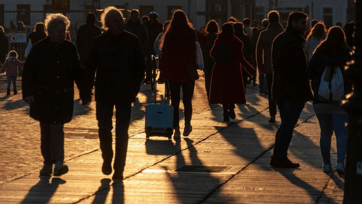 Silhouetted pedestrians walk on a city street at sunset, capturing long shadows and golden light.