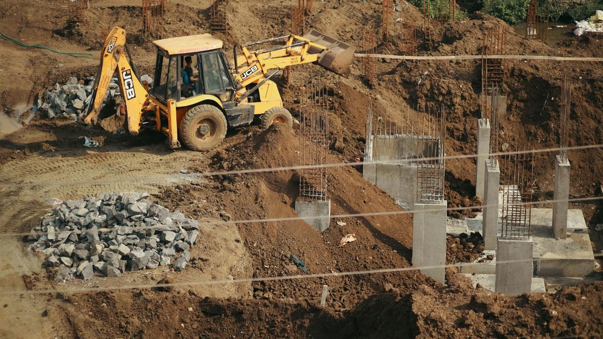 A bulldozer moves soil at a busy construction site, surrounded by piles of gravel and concrete structures.