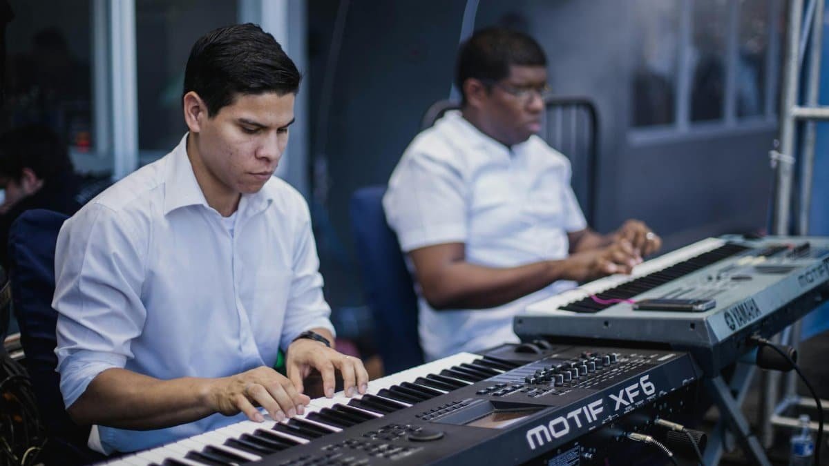 Two musicians focused on playing keyboards in a music studio setting.