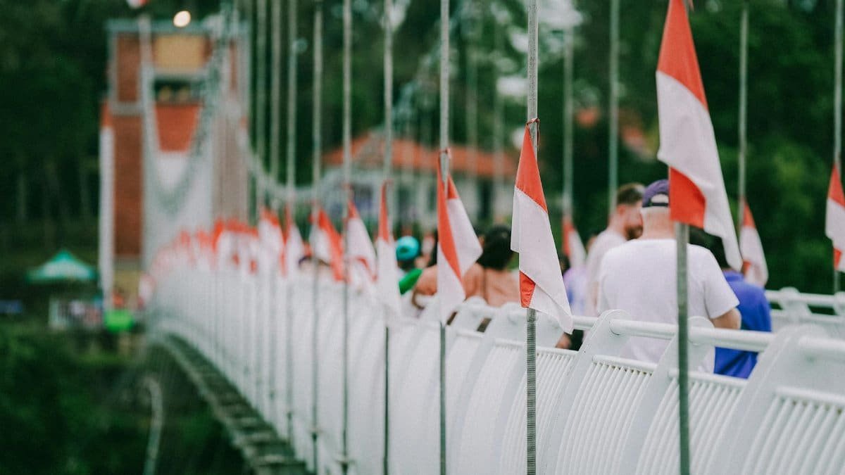 Tourists walk on a suspension bridge adorned with Indonesian flags, highlighting a popular attraction.