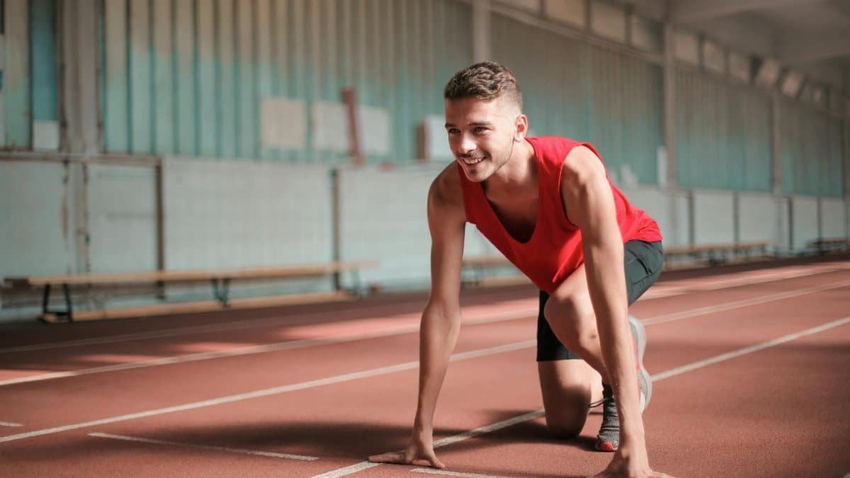 A young male athlete preparing to start running on an indoor track with a smile.